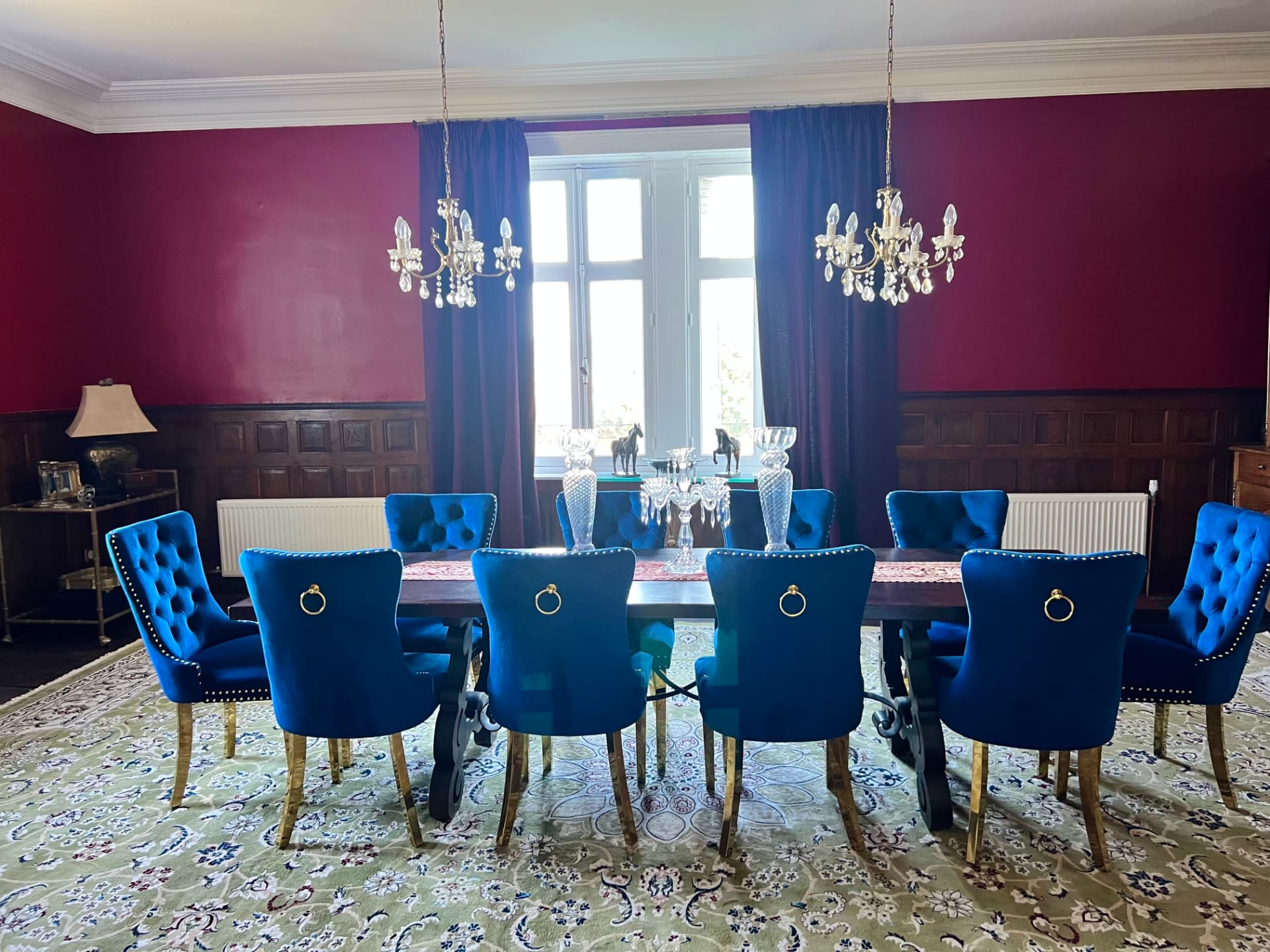 Cobalt blue chairs arranged at the long dining table before deep red walls and dark curtains