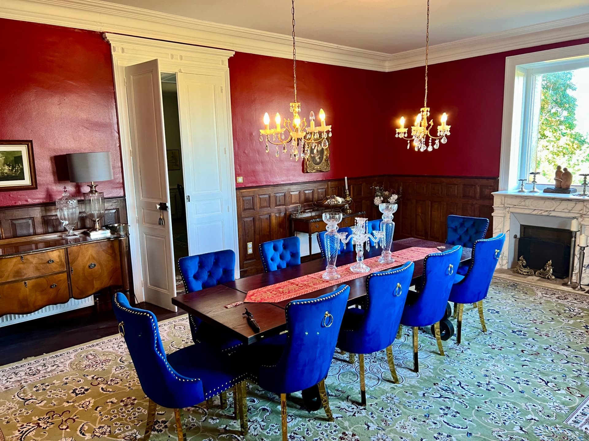 The château dining room with cobalt blue chairs at the long table against deep red walls