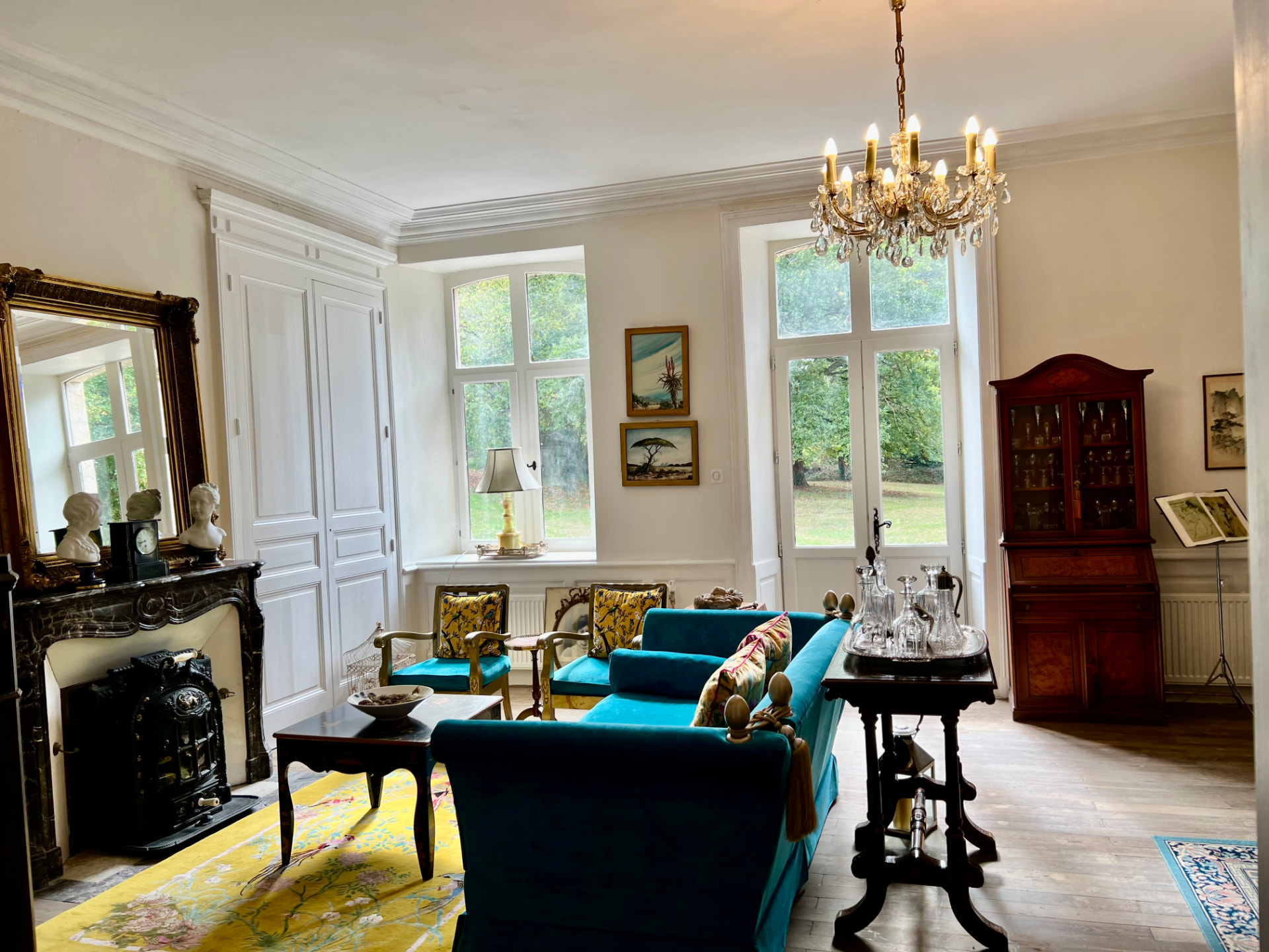 The grand salon of Château Mas Levrault with teal sofas, marble fireplace and crystal chandelier