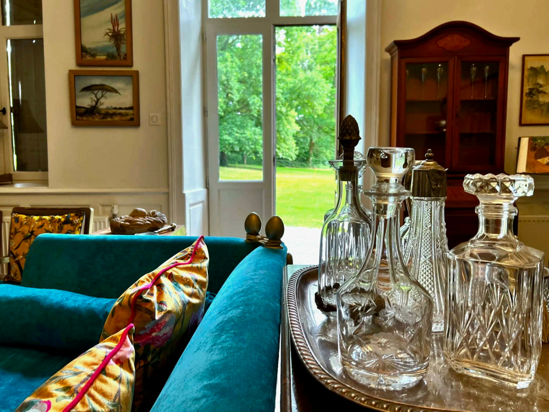 Crystal decanters on a silver tray in the château salon, with the garden beyond