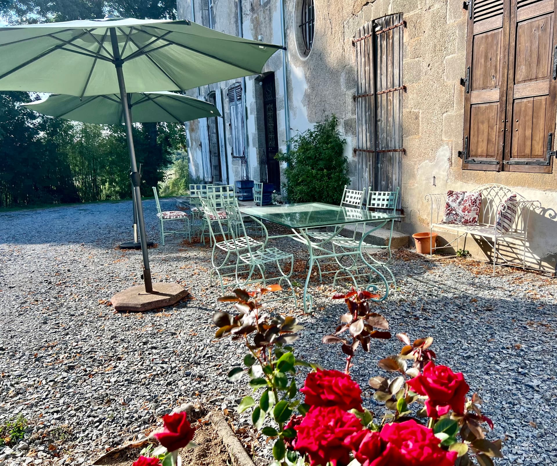 The garden terrace beneath a green umbrella, with wrought-iron chairs and red roses beside the château